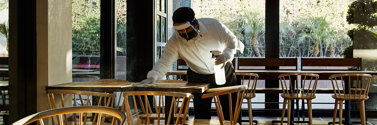 Masked restaurant employee cleans tables