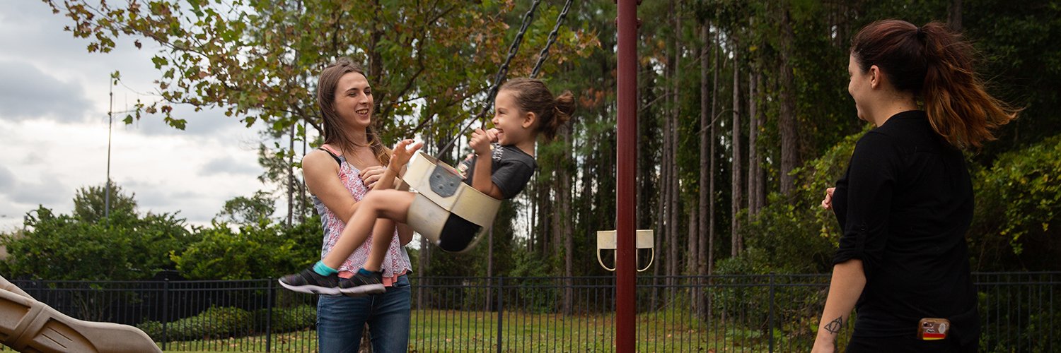 Mother pushing daughter on swings set. 