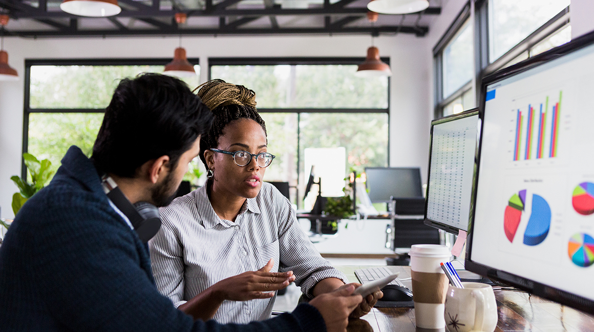 Two people working and looking at graphs on a computer. 