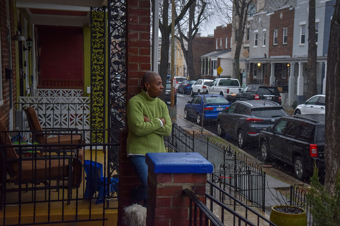 Woman stands on the front porch of her home.