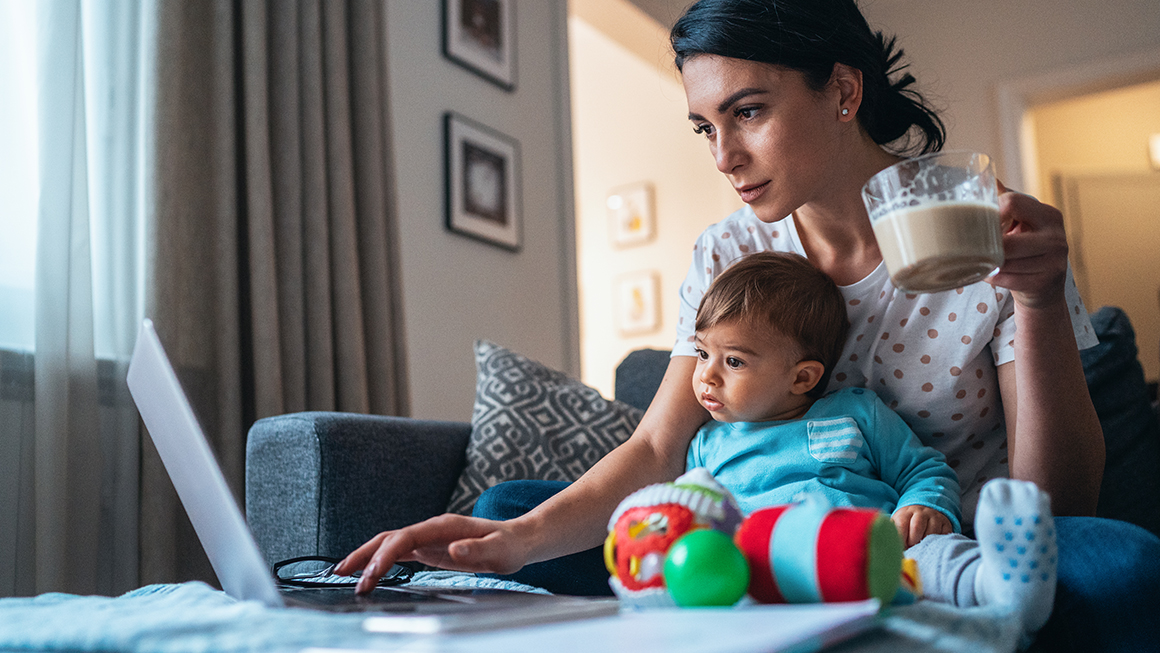 Mother working off a laptop with her child on her lap.