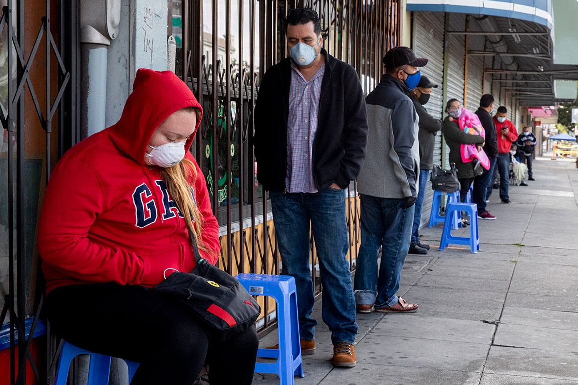 Francisco Montero (center) of Richmond wears a mask while waiting with others in a long line outside of Terra Nova Clinic in the Fruitvale neighborhood of Oakland