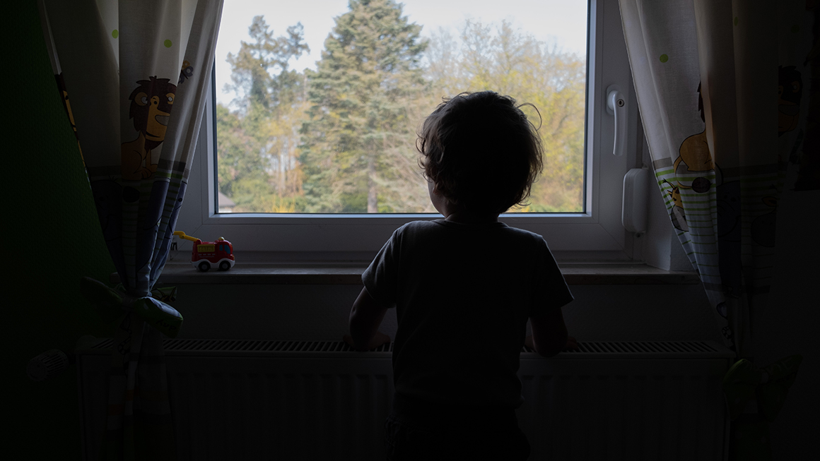 Child in their bedroom looking out their window.
