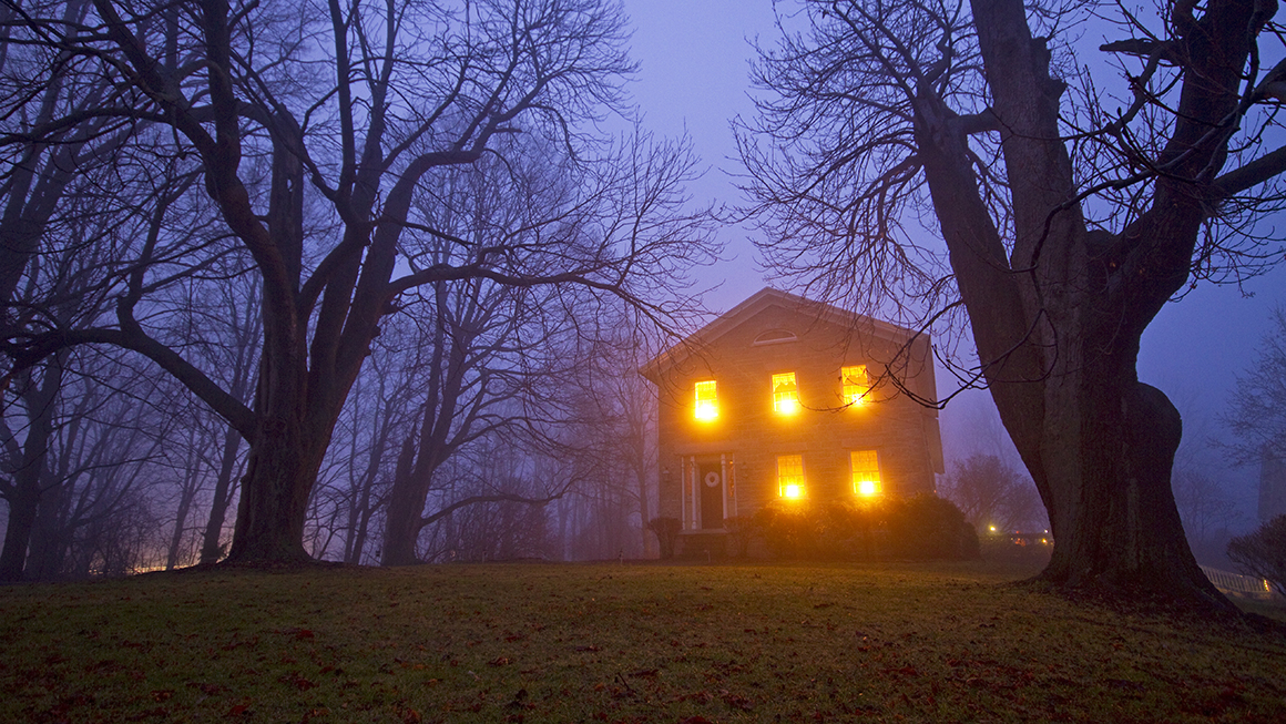 A house with light in the windows sits on the hill in the dark