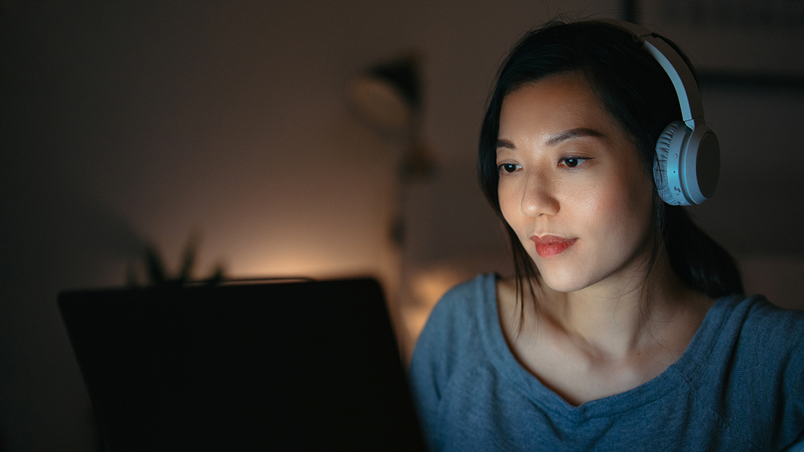 A woman looking at a laptop screen with headphones on. 