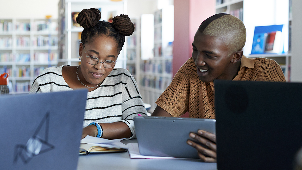 A student and a teacher working together with laptops nearby.