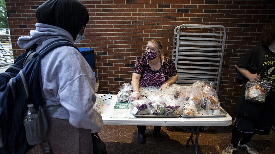 Woman in  a face mask hands out food at school to students.