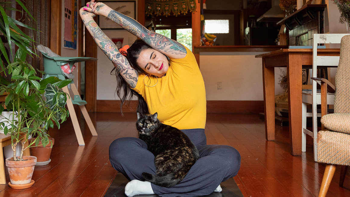 An image of a woman stretching with a cat on her lap. 