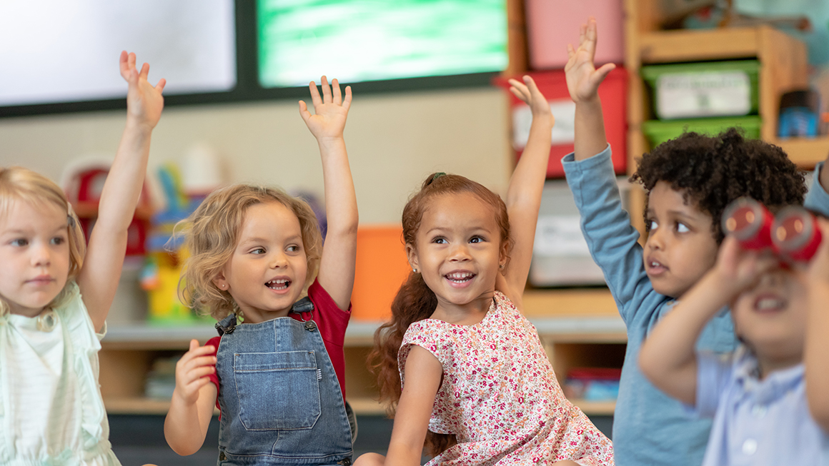 A group of elementary students raising their hands in a classroom