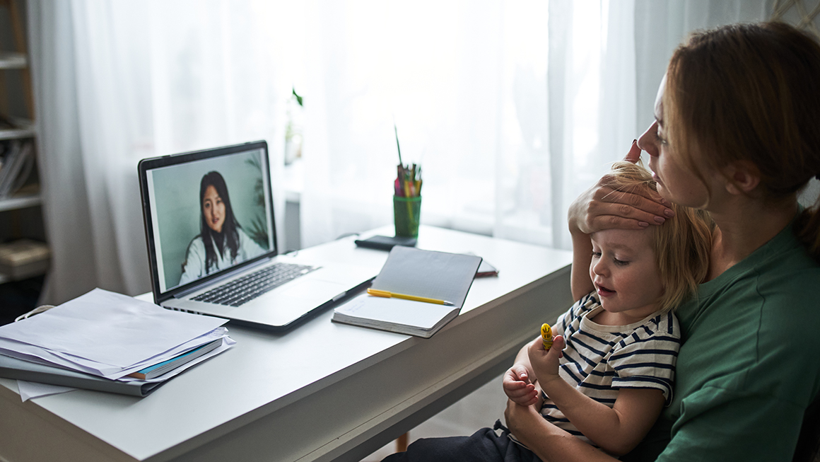A woman holding her child and talking to her doctor through a laptop.