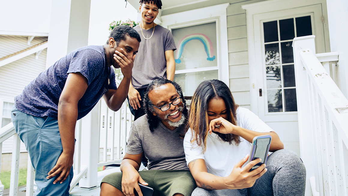 A family on their front steps looking at their mobile phone. 