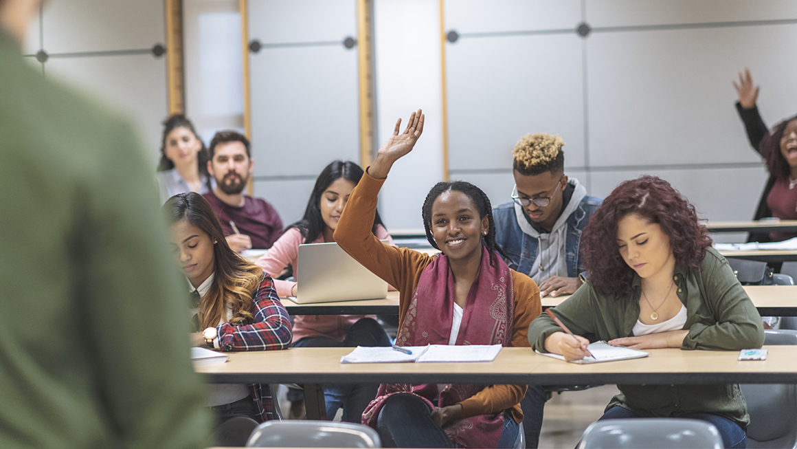 An image of college aged students in a classroom facing the profesor.