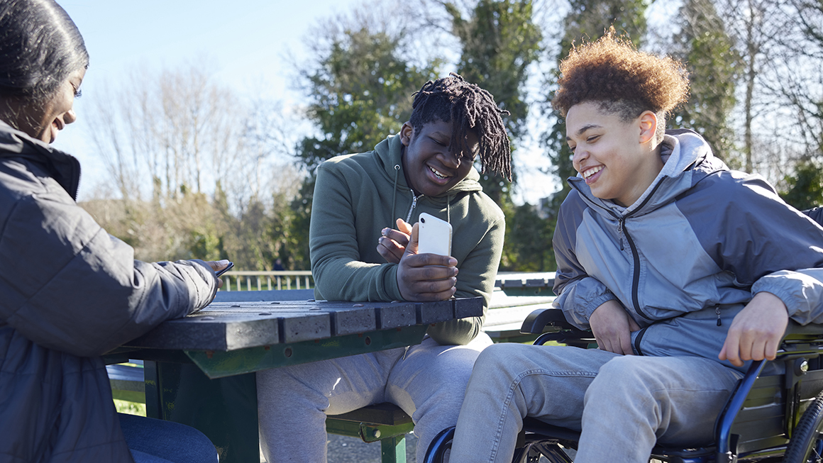 Young boys looking at their phones outside laughing together.