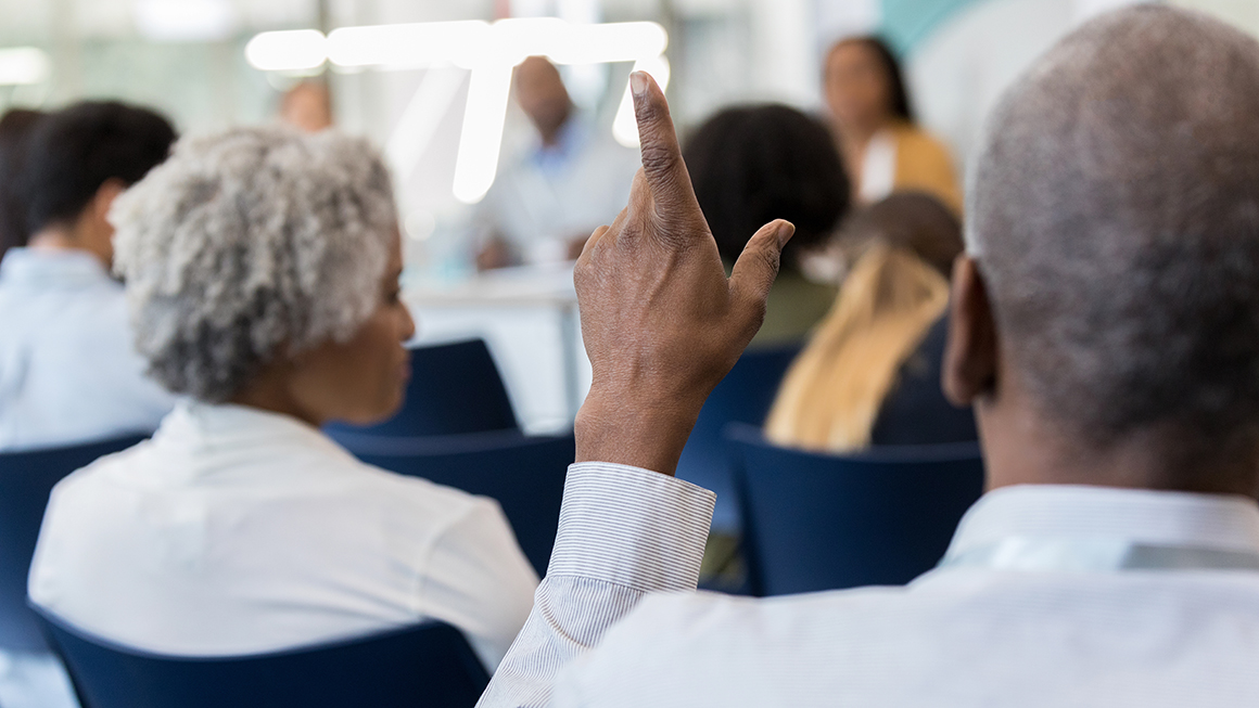 A shot of people sitting in chairs raising their hands.