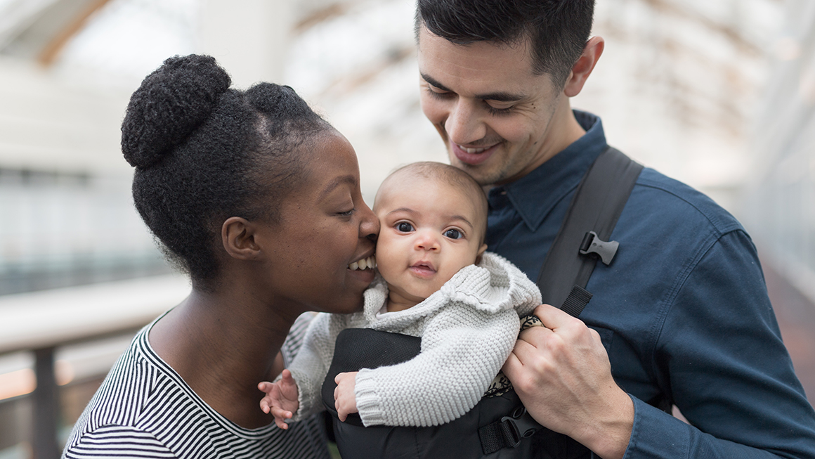 A couple kissing and hugging their baby.