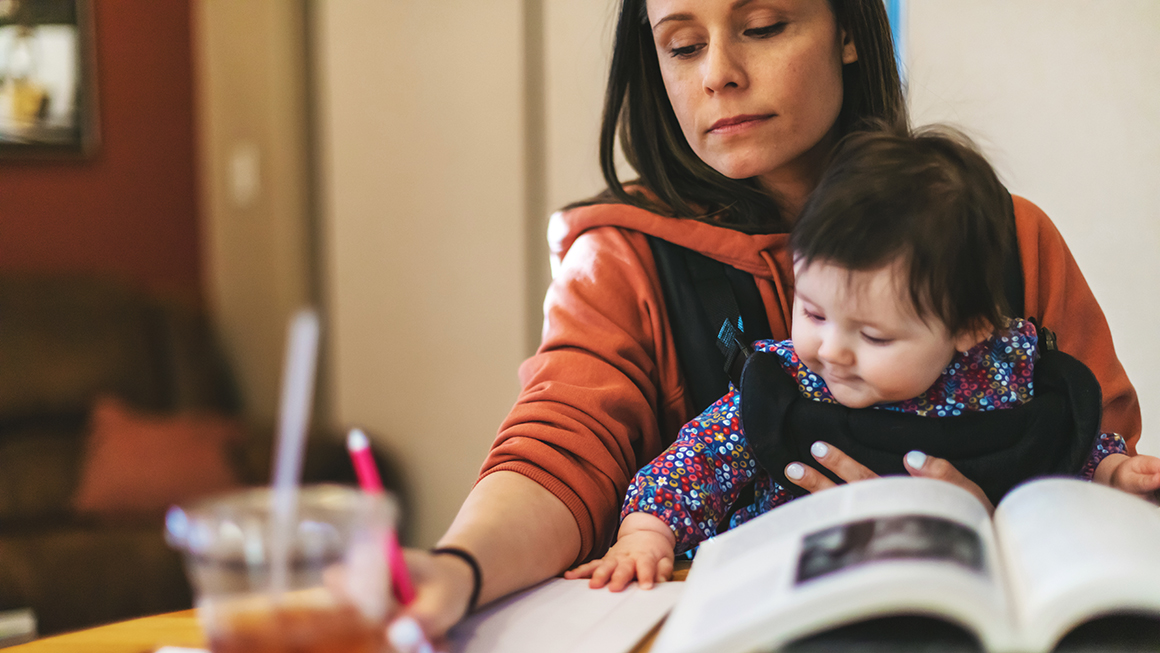 A mother and her child strapped to her front sitting at a table.