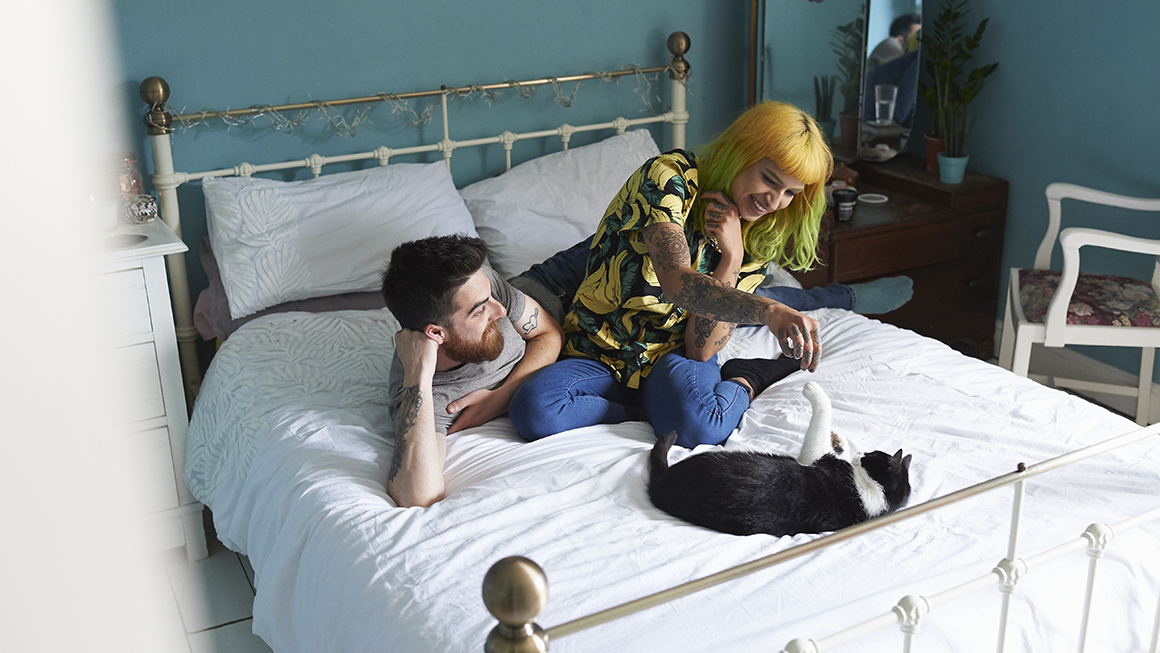 Two young adults on a bed playing with a cat.