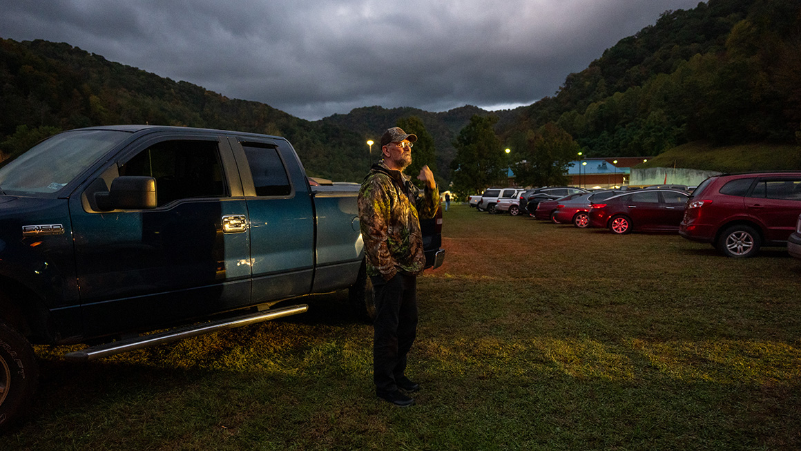 A man outside in a field next to a parked truck.