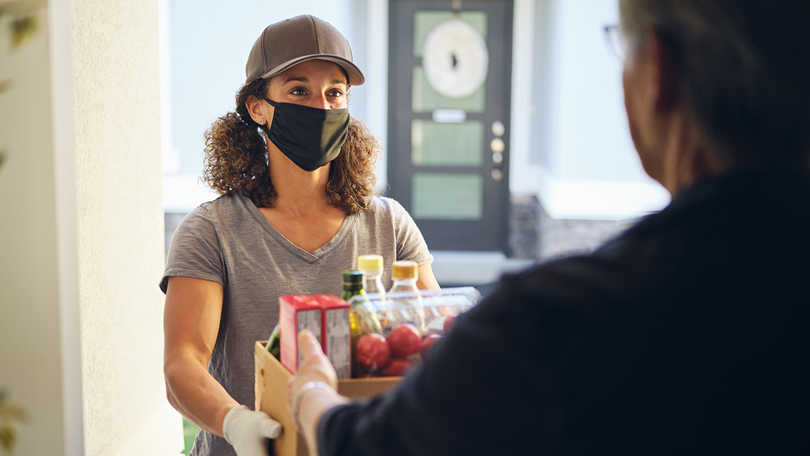 A woman wearing a mask delivering groceries.