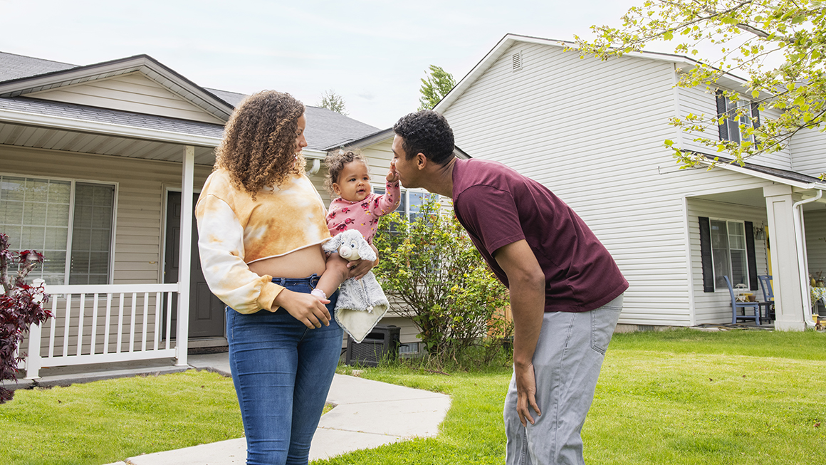 A young couple and their baby in front of their home.