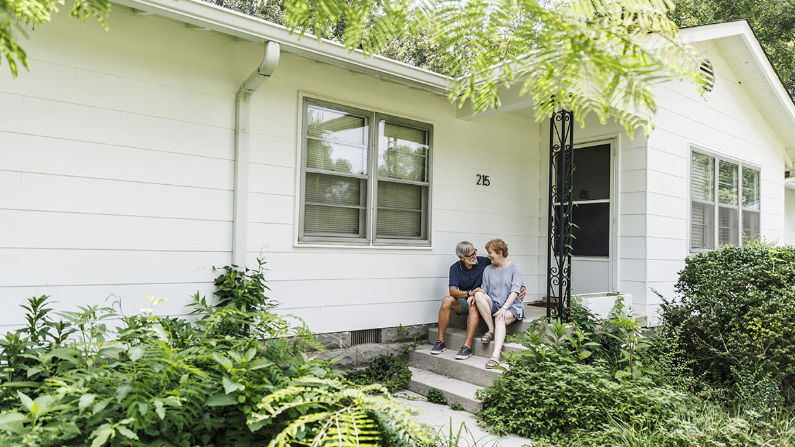 An older couple sitting on the steps of a single family home.