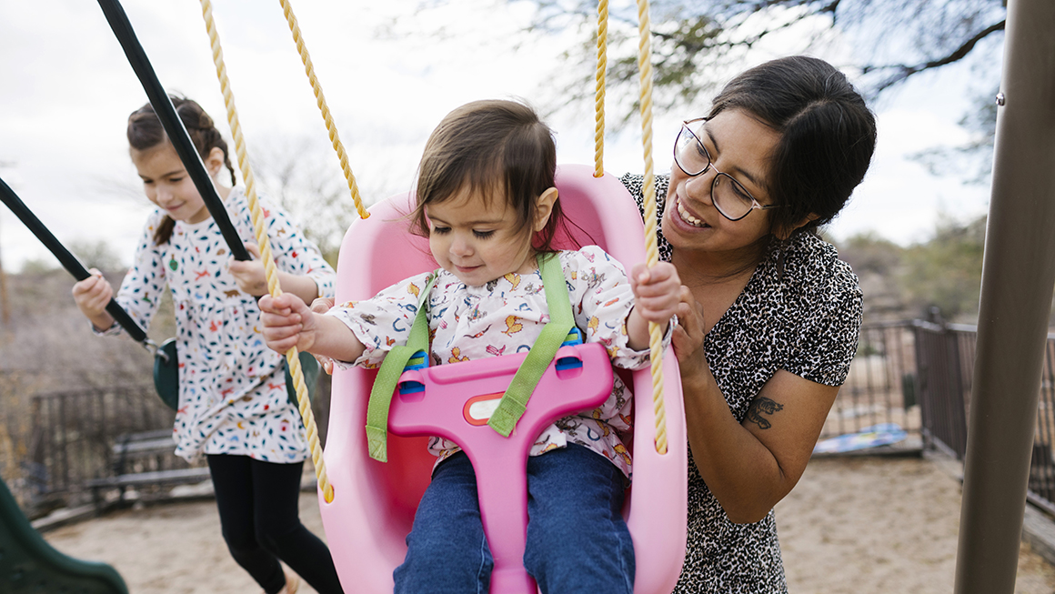 image of child being pushed on swing by caretaker