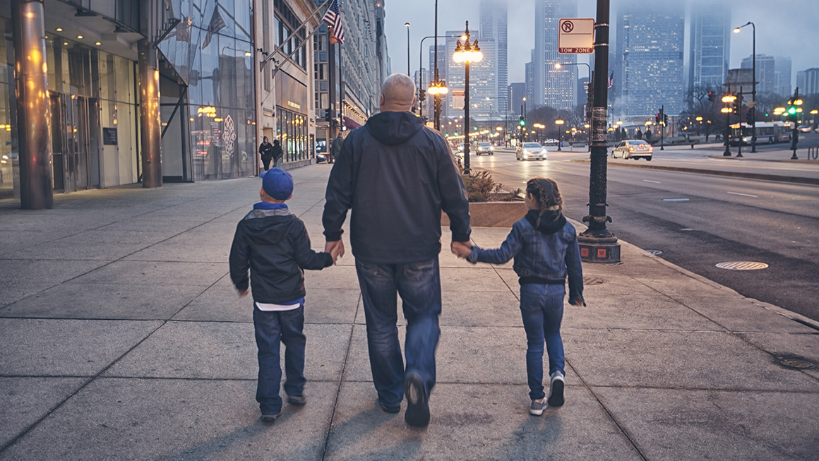 photo of father holding hands with children walking on sidewalk