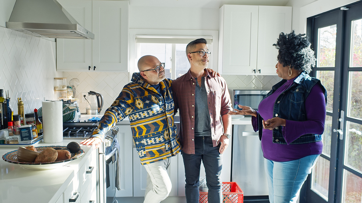 photo of male couple in kitchen talking to another person