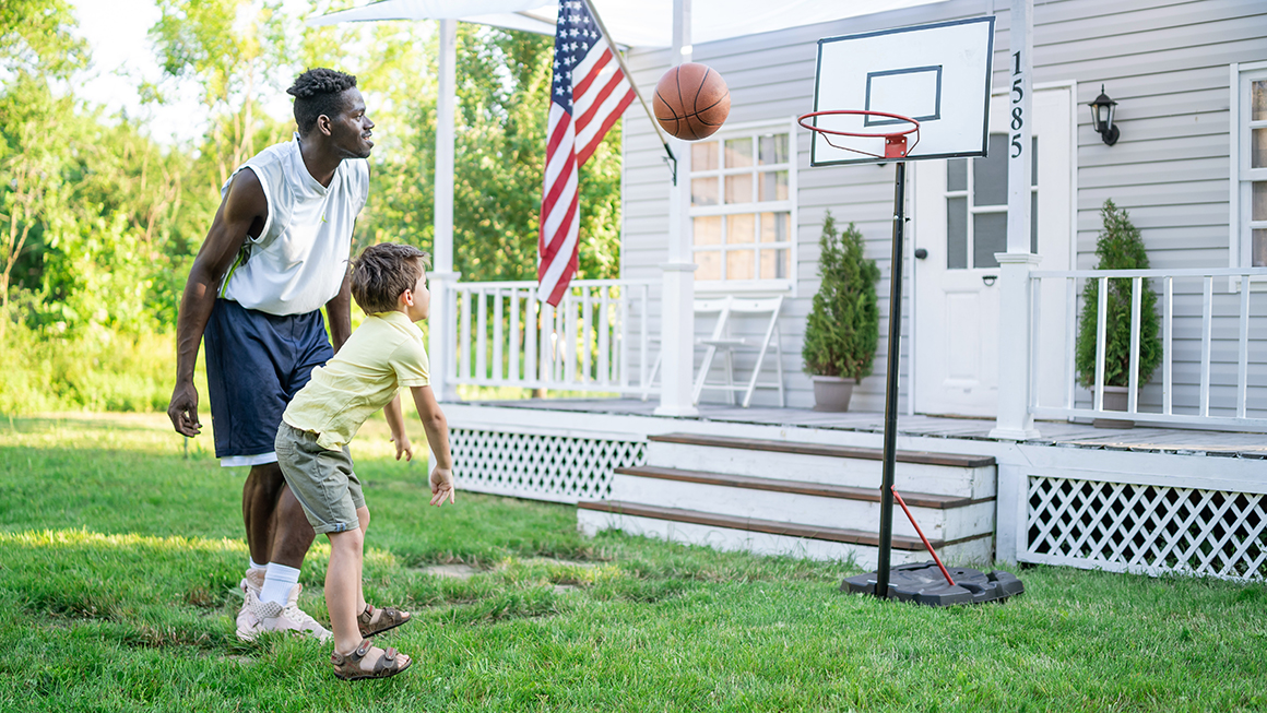 photo of father playing basketball with child outside of house