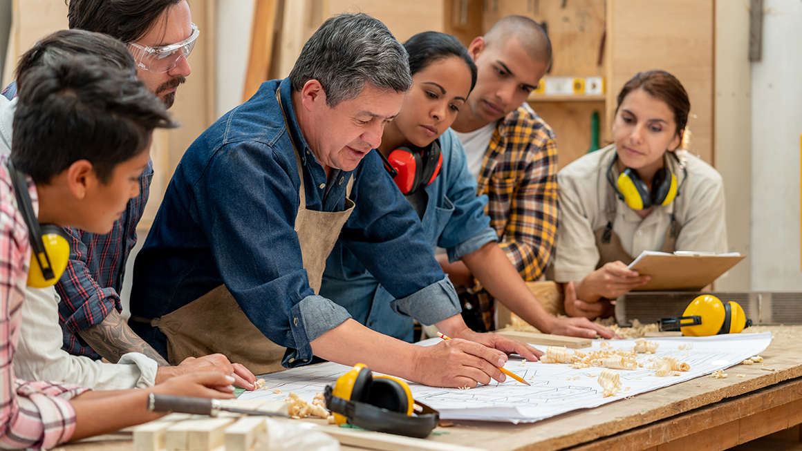 photo of Group of Latin American workers at a factory making furniture and looking at a blueprint - manufacturing concepts