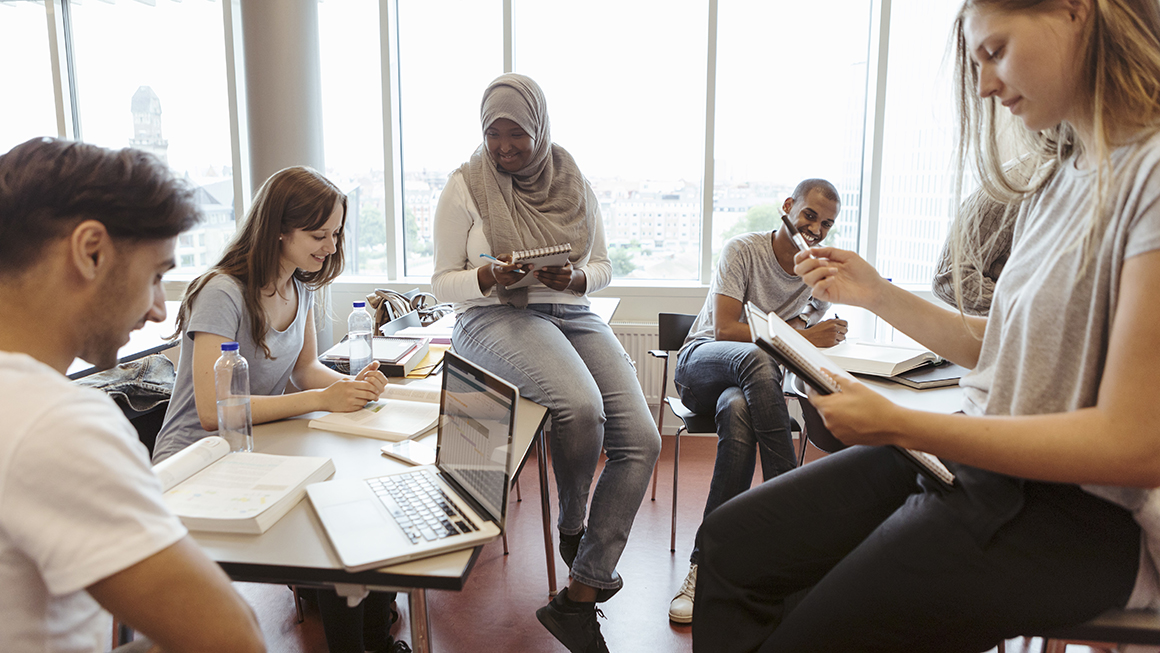 photo of smiling multi-ethnic friends discussing over project in classroom at university