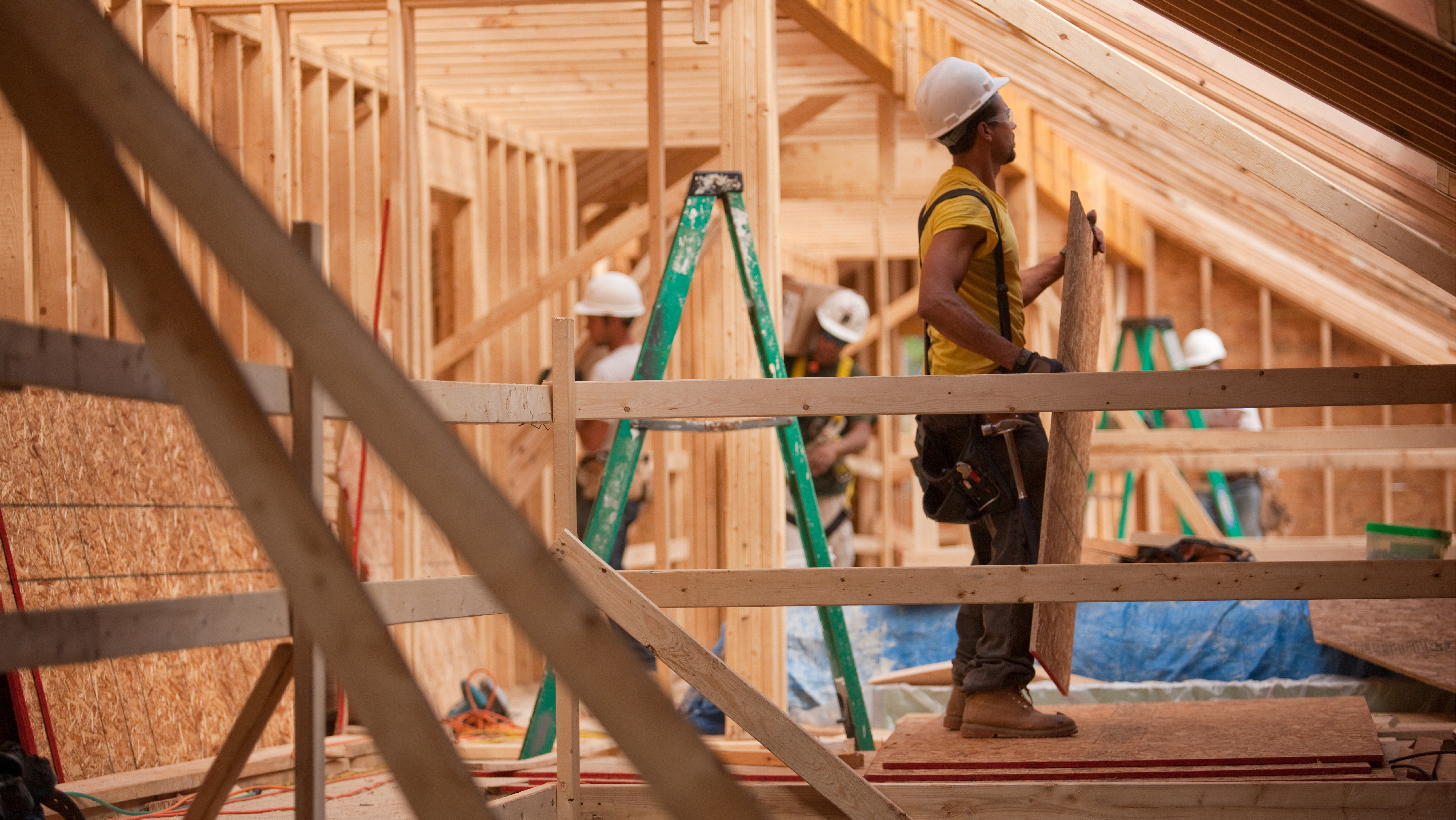 photo of Hispanic carpenters bringing sheathing to roof at a house under construction