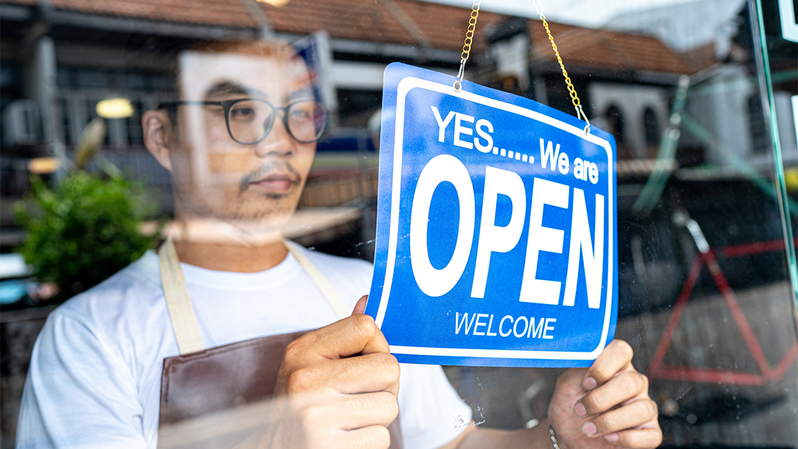 A worker hanging a sign indicating that they are open. 