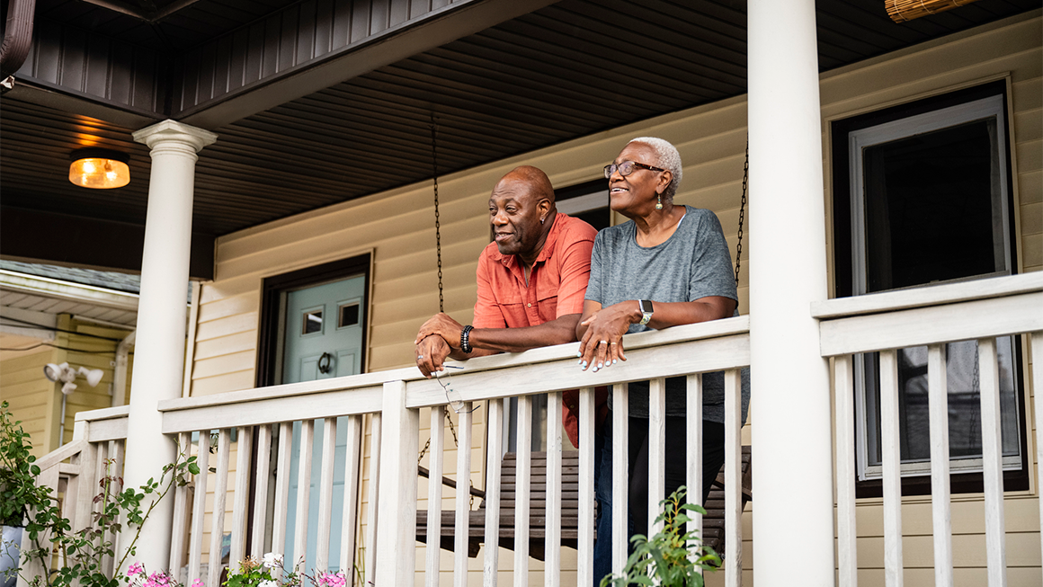 An image of an older couple on the front porch of their house.
