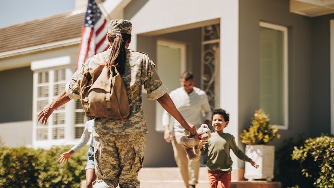 Photo of a young army veteran returning home to her family. She extends her arms to her children as they run towards her.