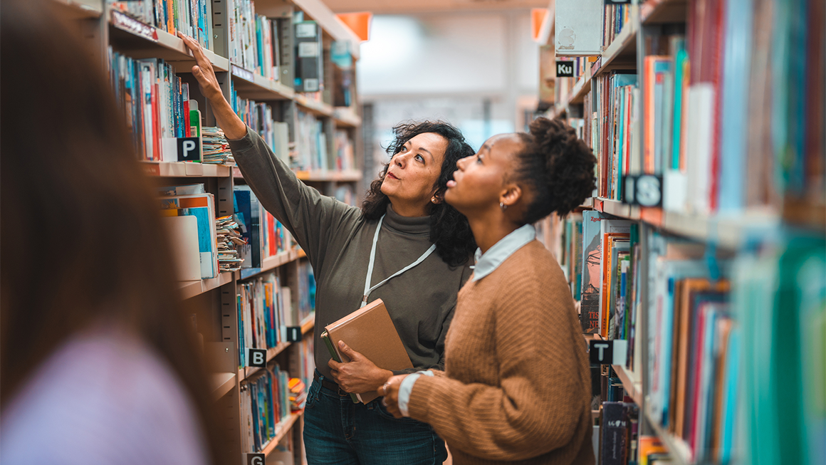 Two women in a library looking at books.