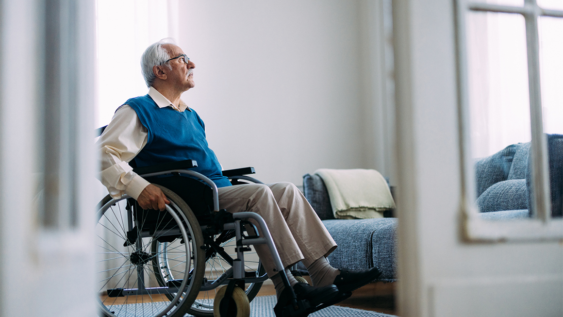 An older man in a wheelchair looks out his window.