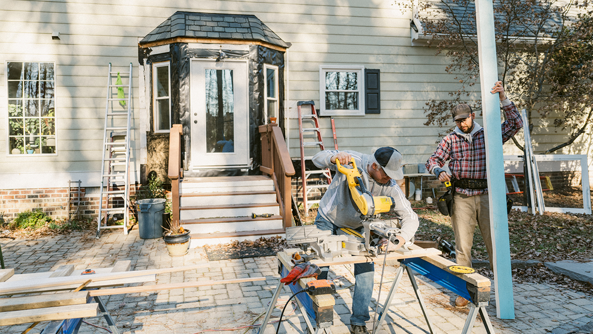 Photo of two construction workers repairing the siding around a house's back door. 