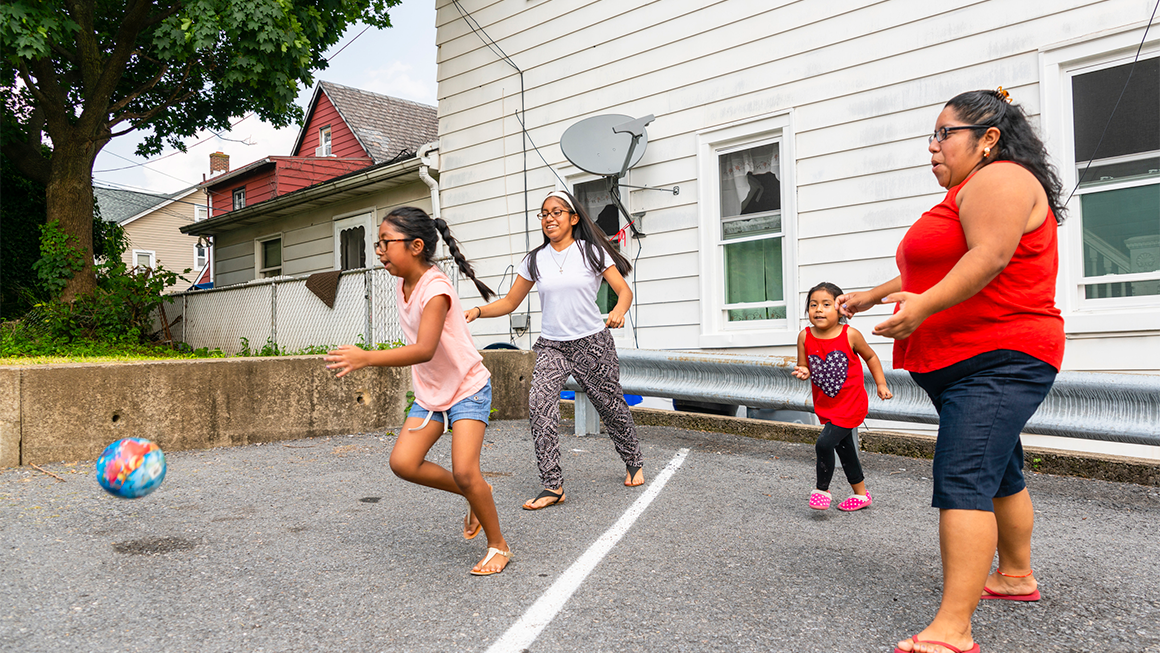 An immigrant family—three children and their mom—playing with a ball outside.