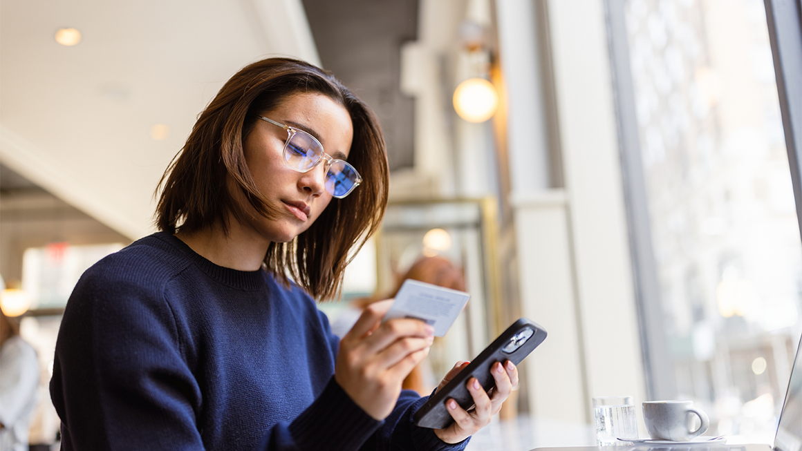 A young woman uses a credit card to make a purchase on her phone.