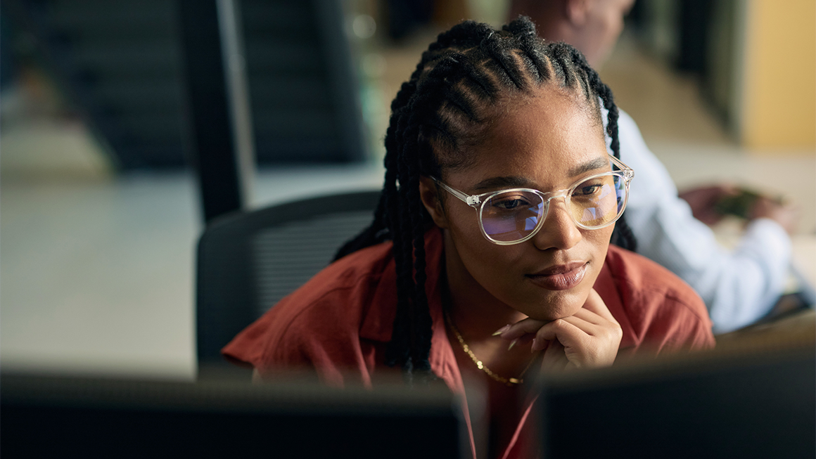 A woman with braids and glasses looks intently at her computer.