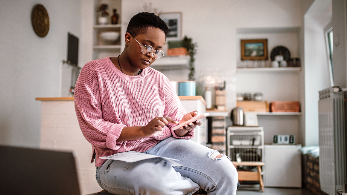 Photo of a young Black woman in a pink sweater reviewing her finances.