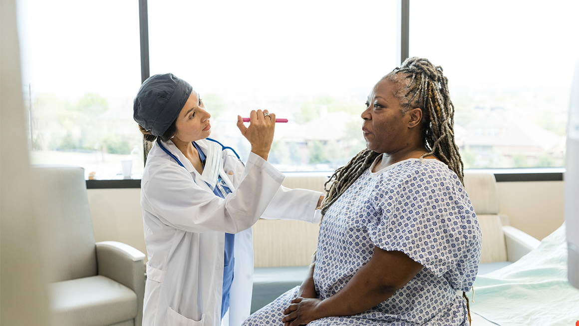 Photo of an older Black woman in a hospital gown having her vitals checked.