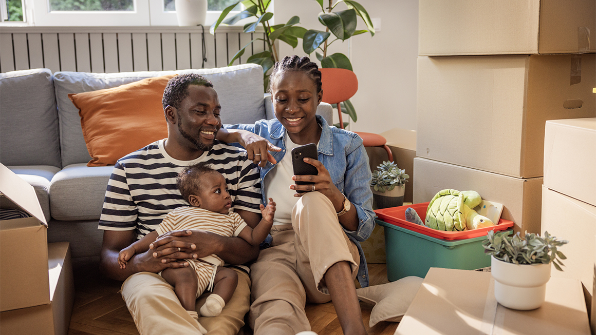 Two parents and their child sit among moving boxes in a new home.