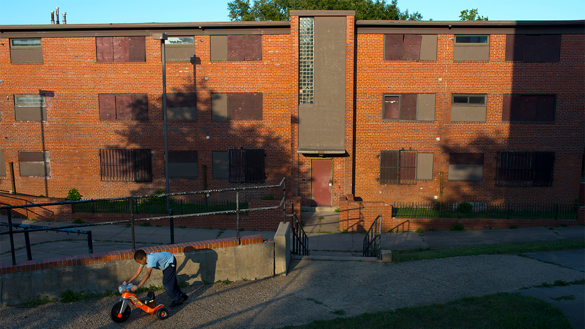 Child plays with a tricycle in front of a public housing building