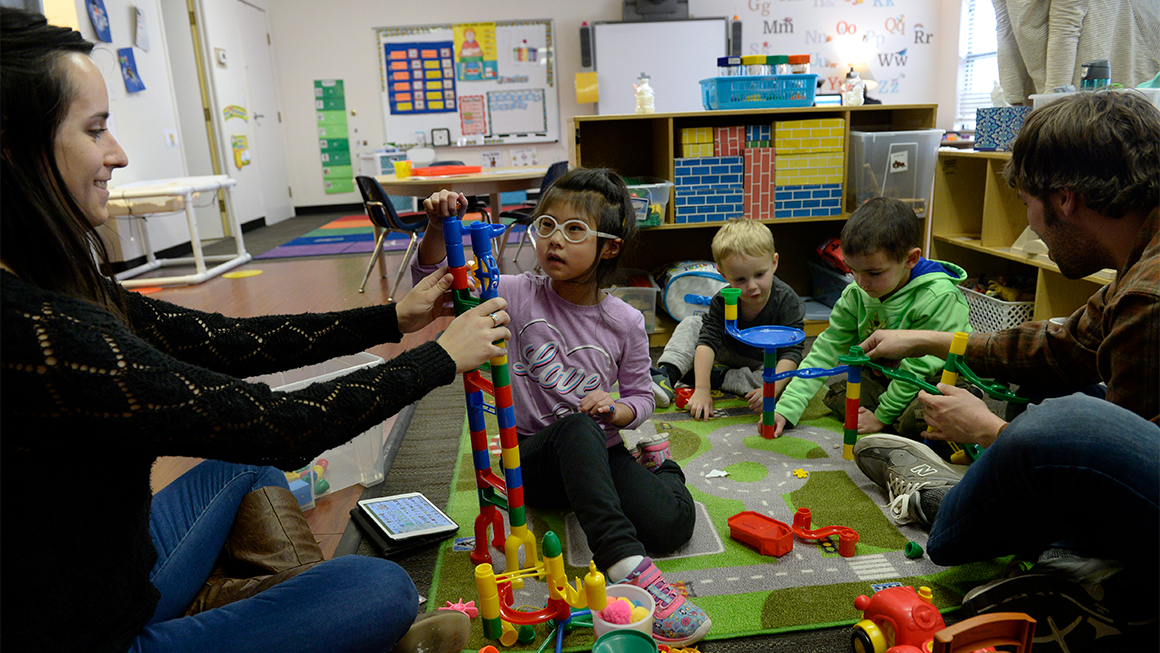 Three young children play with child care providers