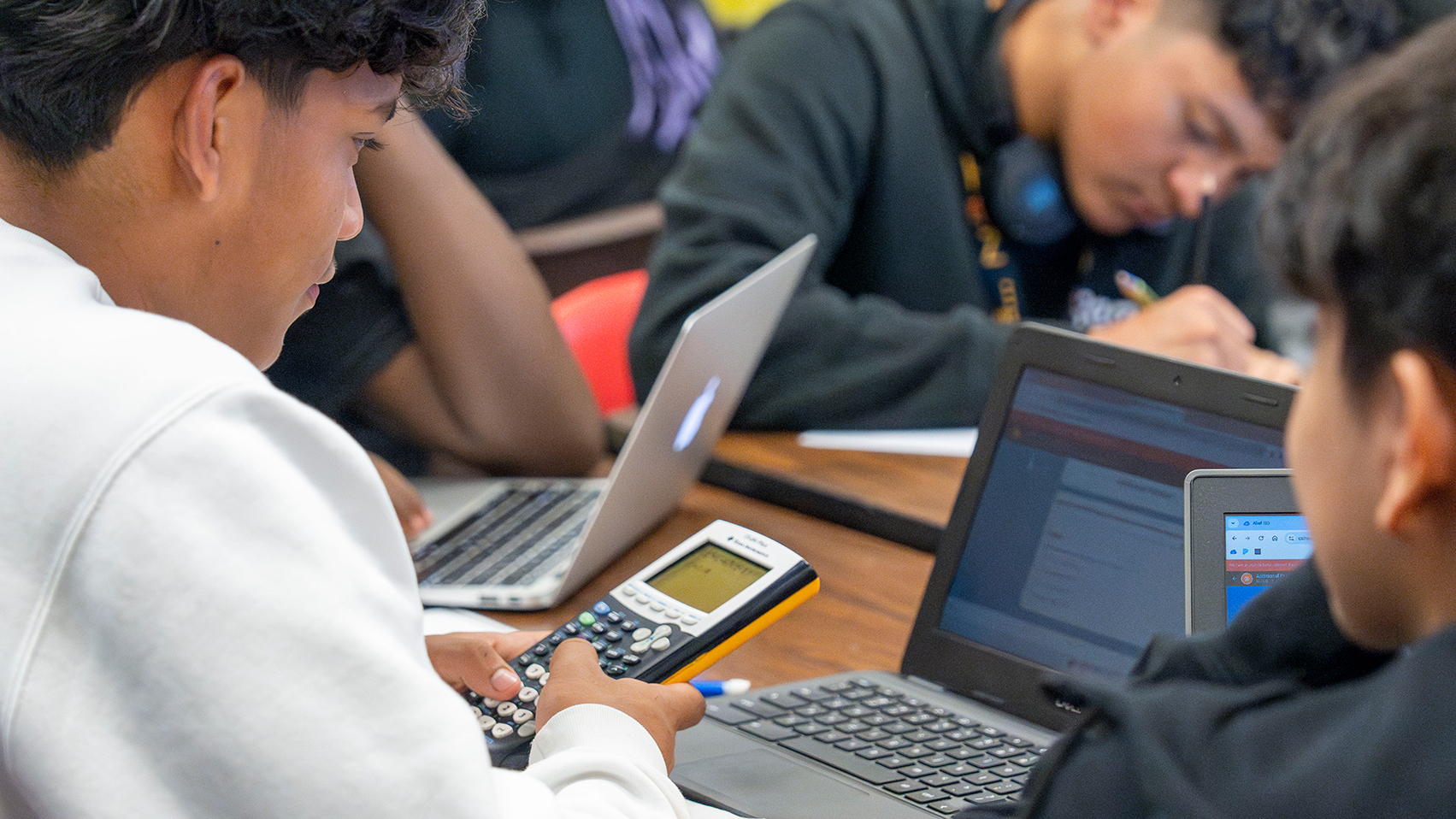 Students using graphing calculcatiors and a laptop while in a classroom