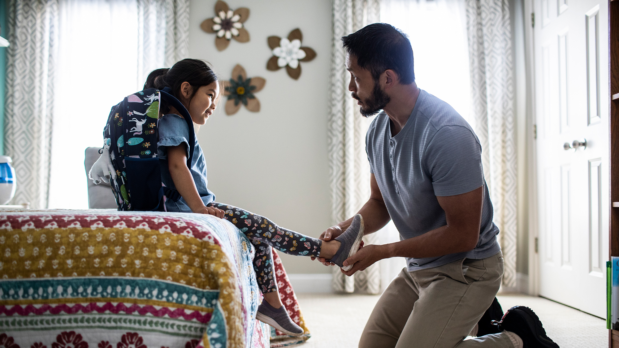 Photo of a father helping his daughter put on her shoes before school. 