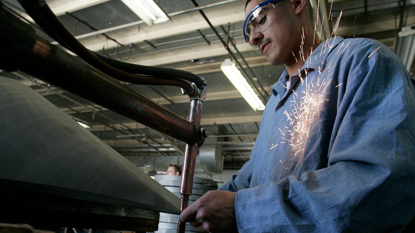 A man wearing safety glasses and a blue uniform works in a factory