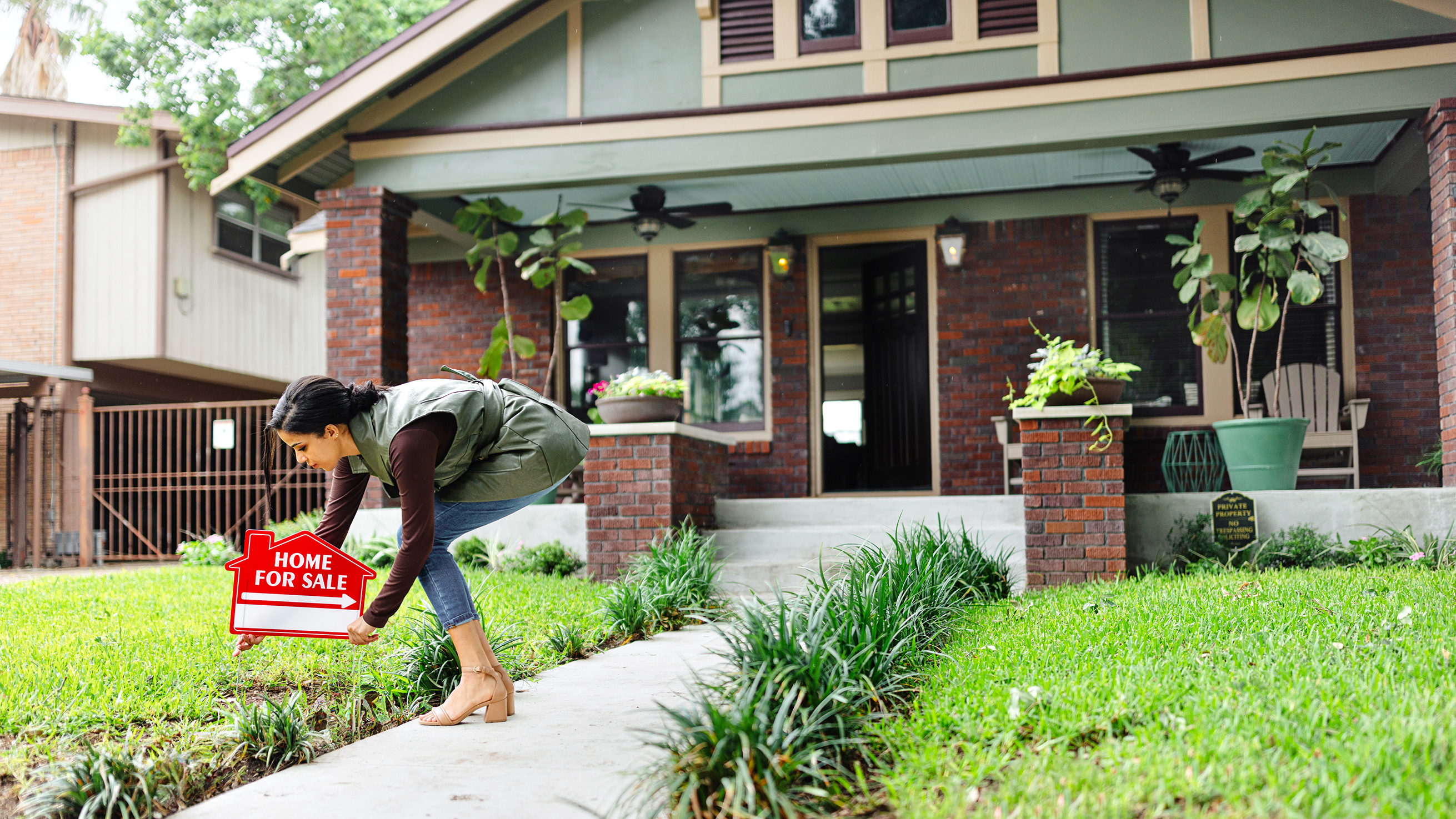 A real estate agent places a for sale sign in front of a home.